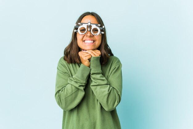 孤立した壁の上の若い眼科医の女性は、あごの下に手を保ち、幸せそうに脇を見ています