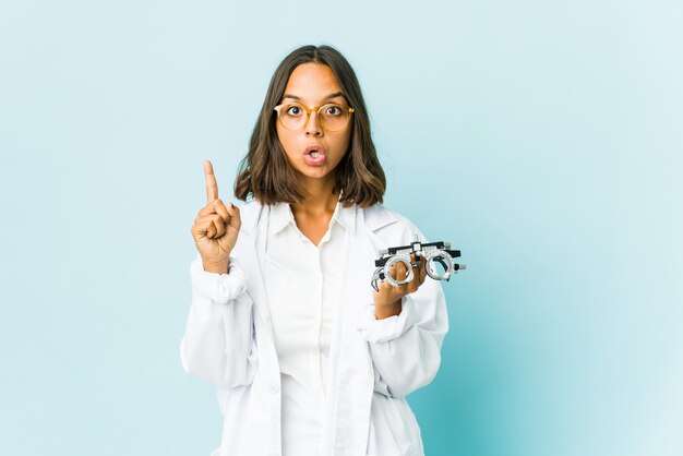 Young oculist woman over isolated wall pointing upside with opened mouth