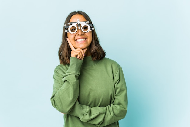 Young oculist woman over isolated wall smiling happy and confident, touching chin with hand