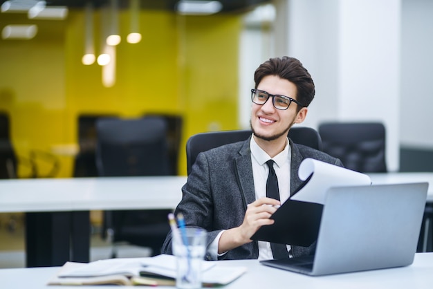 Young office worker in glasses reads documents in the office. Young business manager working with new startup project.