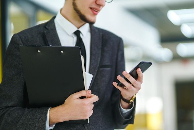 携帯スマートフォンを使用して眼鏡をかけている若いサラリーマンビジネスマンは手に電話を持っています