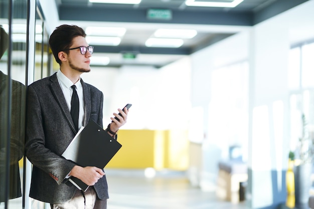 Young office worker in glasses using mobile smart phone. Businessman holds telephone in hand.