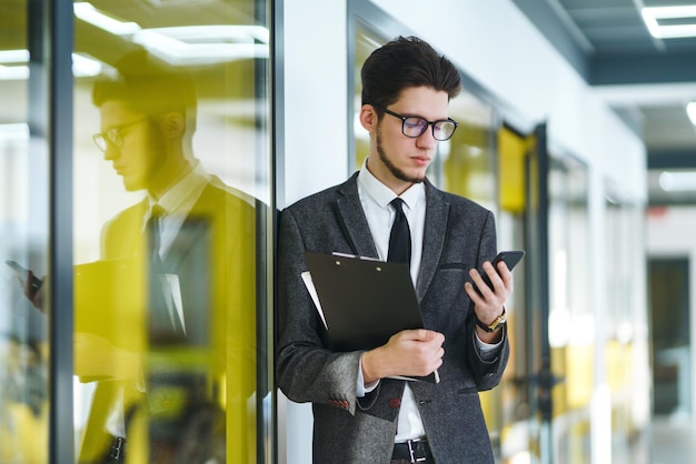 Young office worker in glasses using mobile smart phone Businessman holds telephone in hand