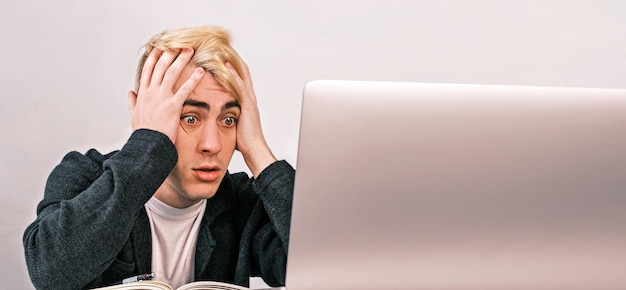 Young office worker shocked and surprised looking into laptop clutching his head