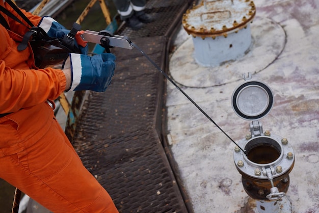 Young offshore engineer sounding fuel oil cargo tank on cargo\
deck on supply vessel in harbor