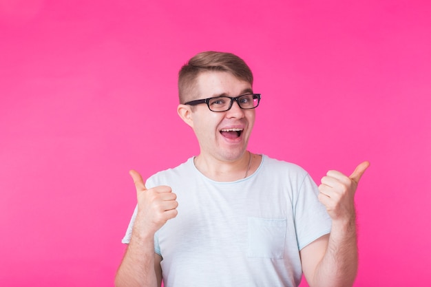 Young optimistic man on pink showing thumbs up with positive emotions of content and happiness