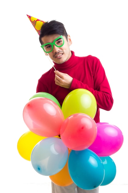 Young optimistic man with celebrating hat holding many colored balloons and card stick of glasses