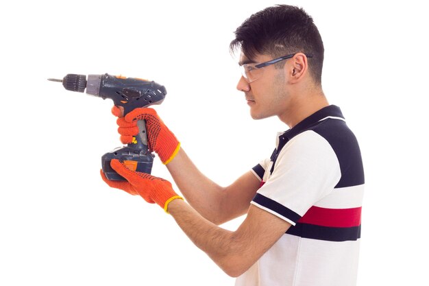 Young optimistic man with orange gloves and protective glasses holding grey electric screwdriver