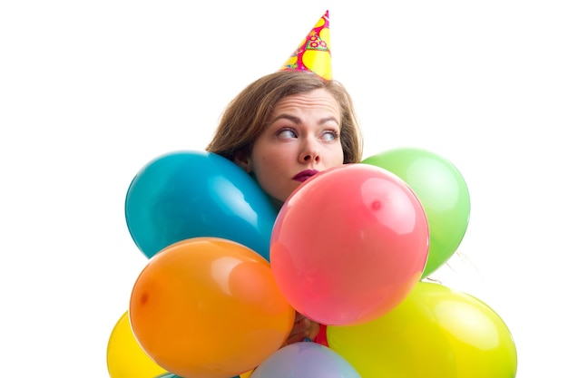 Young optimistic woman with celebrating hat holding many colored balloons and card stick of glasses