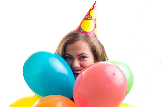 Young optimistic woman with celebrating hat holding many colored balloons and card stick of glasses