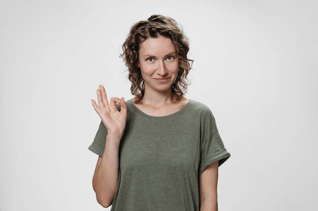 Foto la giovane donna ottimista con i capelli ricci dimostra il segno giusto