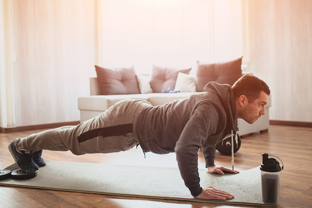 Young ordinary man doing sports at home. Plank position on his fists or doing push ups.