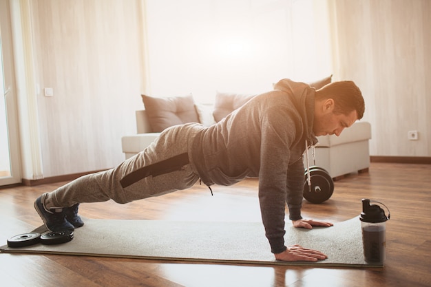 Young ordinary man doing sports at home. Plank position on his fists or doing push ups.