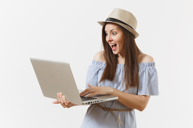 Young overjoyed woman in blue dress, hat working on modern laptop pc computer isolated on white background. People, freelance business, lifestyle, online shopping concept. Mobile Office. Advertising.