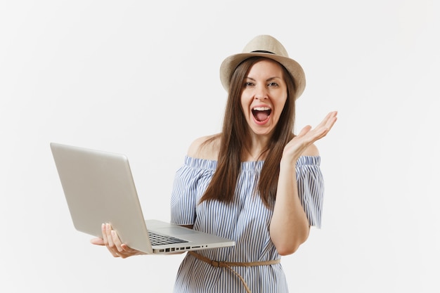 Young overjoyed woman in blue dress, hat working on modern laptop pc computer isolated on white background. People, freelance business, lifestyle, online shopping concept. Mobile Office. Advertising.