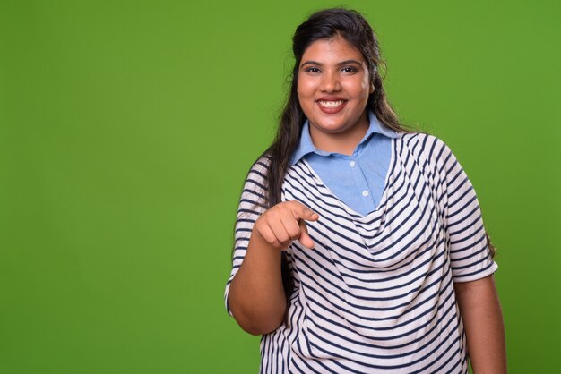 Young overweight beautiful Indian businesswoman against green wall