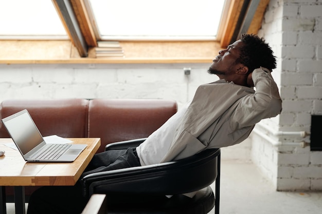 Young overworked african american businessman sitting in leather armchair