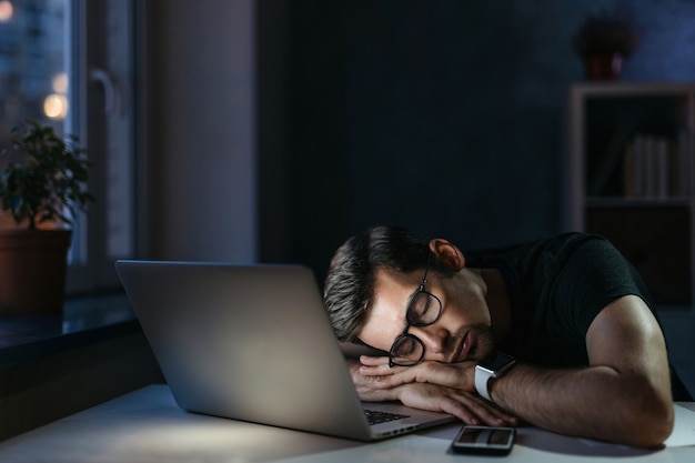 Young overworked distressed businessman freelancer fell asleep at workplace while working remotely over hours