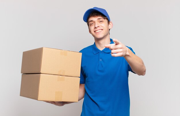 Young package deliver boy pointing at camera with a satisfied, confident, friendly smile, choosing you