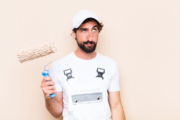 Young painter bearded man holding a paint roller with angry expression