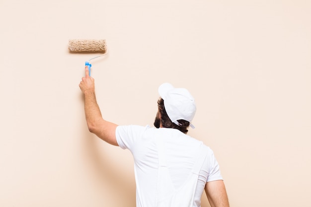 Молодой художник бородатый мужчина красит стену валиком