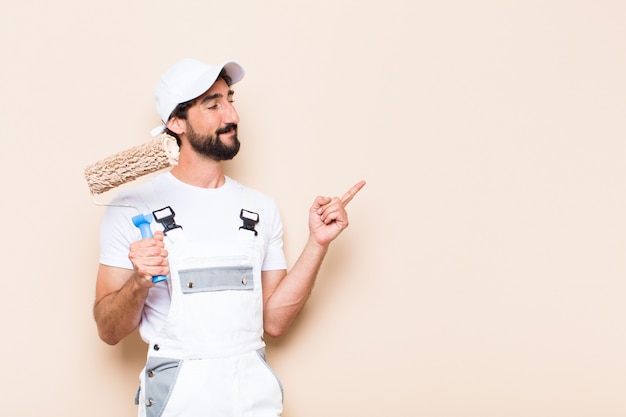 Photo young painter bearded man pointing expression and holding a roller