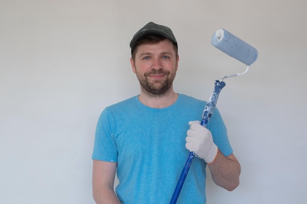 Young painter in blue tshirt cap and gloves painting a wall with paint roller