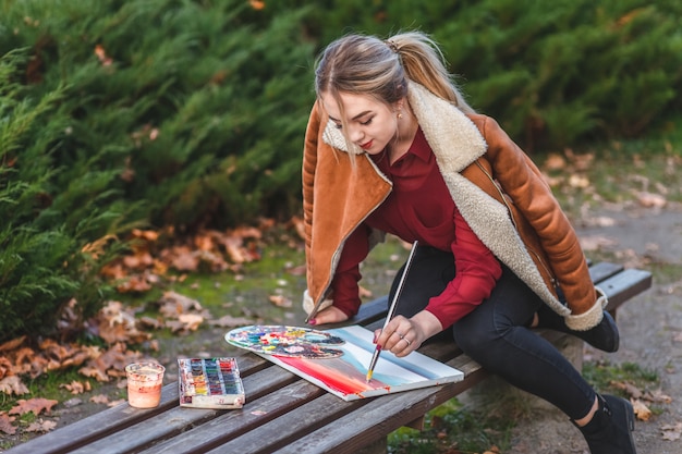 Young painter draws a picture sitting in a park on the bench
