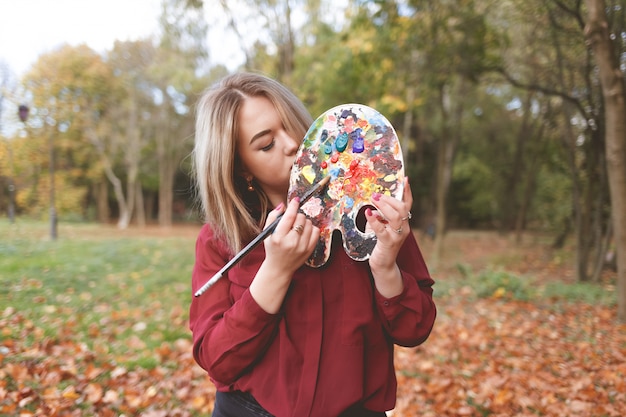 Young painter mixes paints on a palette that she holds in her hands.