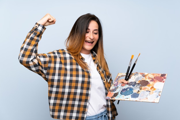 Foto giovane donna del pittore sopra la parete blu isolata che celebra una vittoria