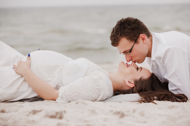 Young parents are expecting a baby lying on the sand by the sea