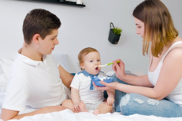 Young parents feed baby on a white background. Happy family .