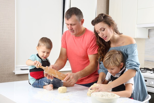 I giovani genitori aiutano i figli piccoli a impastare la pasta sul tavolo della cucina