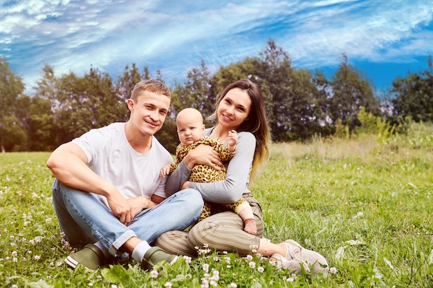 Young parents in their s with six month old baby are sitting on grass of backyard lawn of country