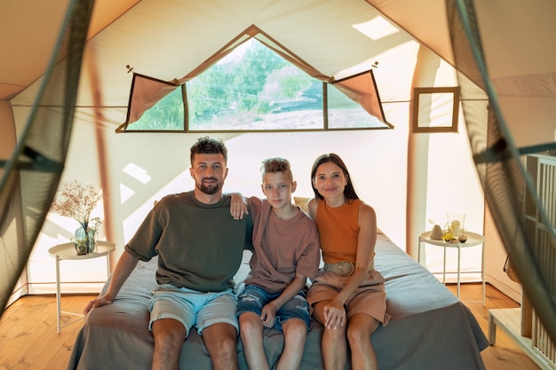 Young parents and their teenage son relaxing in glamping house