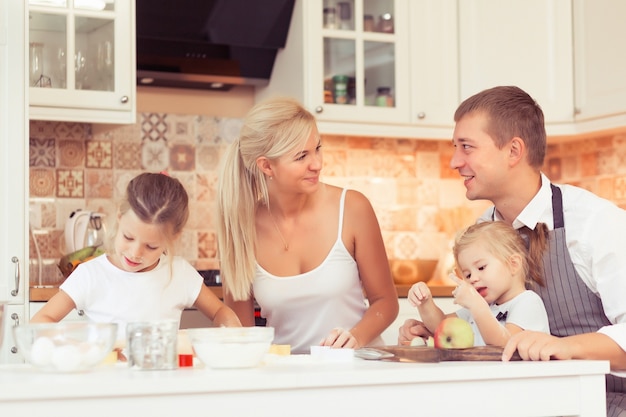 Young parents and their two beautiful and cute children girls cooking and eating breakfast