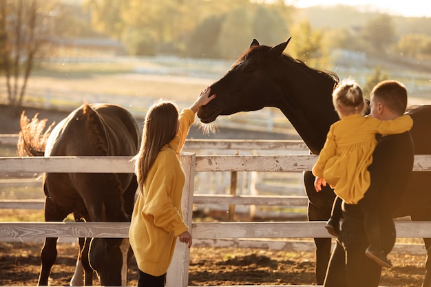 I giovani genitori camminano con la piccola figlia vicino ai cavalli nella sosta di autunno.
