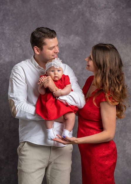 Young parents with a little daughter in their arms Family portrait Mom and baby in a red dress