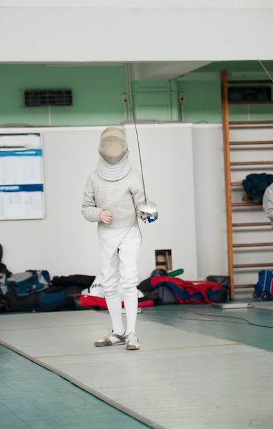 Young participant of the fencing tournament with rapier in hand ready for fight