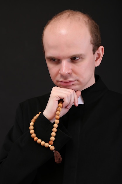 Young pastor with wooden rosary, isolated on black