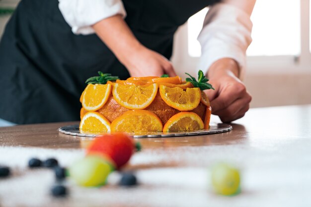 Young pastry chef cooking an orange cake with sliced oranges