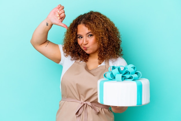 Young pastry latin woman holding a cake isolated on blue wall feels proud and self confident, example to follow