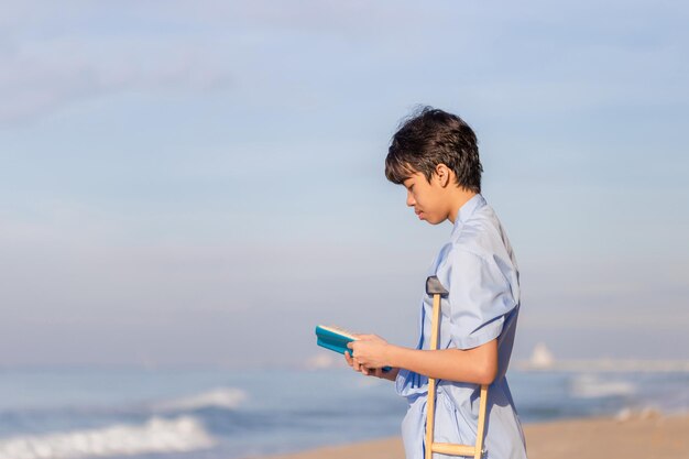 해변에서 책을 읽는 목발을 든 젊은 환자, 해변에서 여행하는 동안 목발을 짚고 있는 장애인.