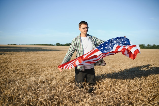 Young patriotic farmer stands among new harvest Boy walking with the american flag on the wheat field celebrating national independence day 4th of July concept