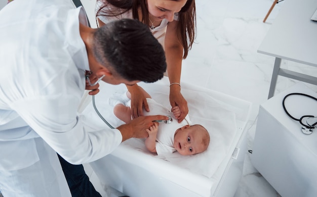 Young pediatrician is with little baby in the clinic at daytime.