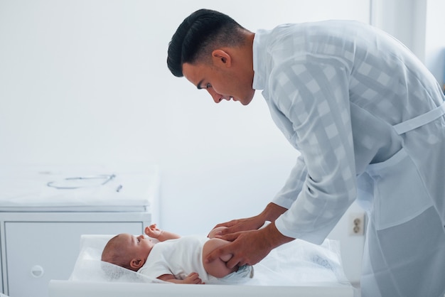 Young pediatrician is with little baby in the clinic at daytime.