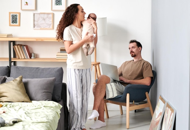 Young pensive man looking at his wife playing with their baby son