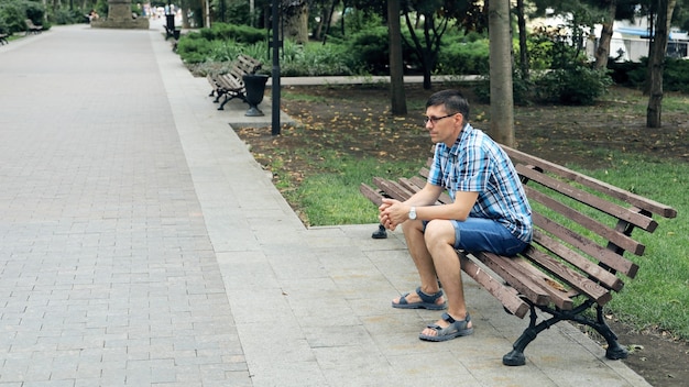 Young pensive man sitting on park bench alone