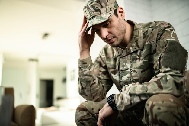 Young pensive military officer feeling sad while sitting alone at home