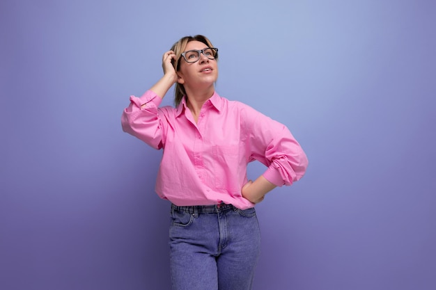 young pensive pretty caucasian blond office worker woman dressed in a pink shirt and jeans and glasses with ponytail hairstyle